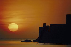 Silhouette of buildings by ocean at sunset