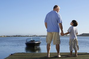 Father and son (6-8) holding hands on jetty, rear view