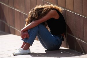 Woman with face down leaning against wall, outdoors