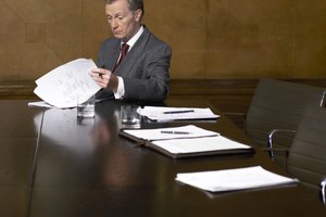 Mature man reading papers at end of table in conference room