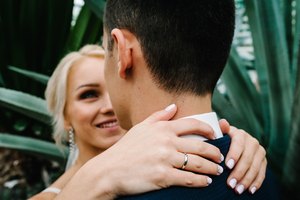 The bride hands hugged the groom's behind his neck. Woman and man in the Botanical green garden full of greenery. Wedding ceremony.